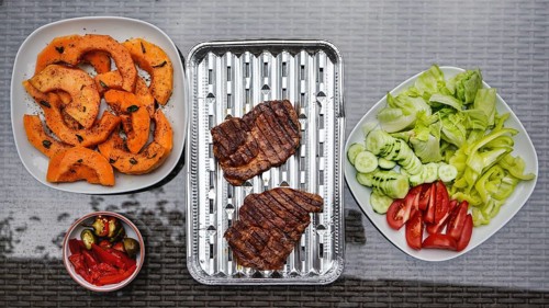 Grilled butternut squash and pork cuts, some fresh vegetable next to it, on glass garden table,