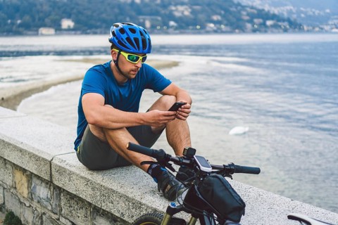 The theme of tourism and travel in Italy. A male cyclist uses a phone on the shore of Lake Como.