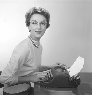 Office girl in the 1950s. A young girl at her typewriter is wearing typical fifties glasses and