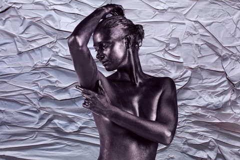 Young beautiful naked woman with glossy skin is posing on the crumpled paper background