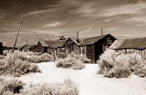 A dusty path between thorny undergrowth leads to poor wooden houses and crooked lamp posts in the