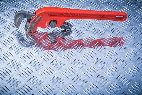 Metal pipe wrench on corrugated metallic background directly above maintenance concept