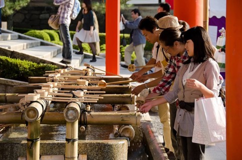 People washing hands at a Tsukubai in front of the Inari Shrine in Kyoto in order to purify