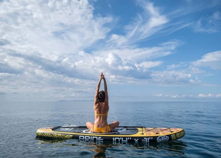Woman practicing yoga on a surfboard under a dramatic sky, Estalella, coast of Llucmajor, Majorca,