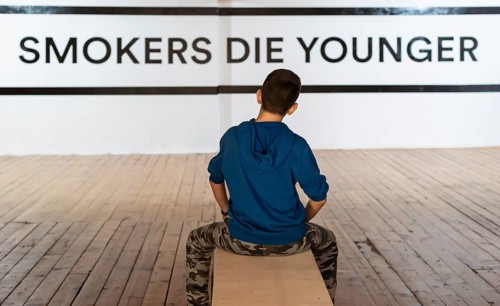 Teenager smoking and message on wall - Smokers die younger. No smoking concept with child. Casual
