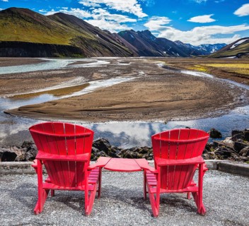 Multi-colored mountains from mineral rhyolite are lit with sun. Two red chaise lounges stand for