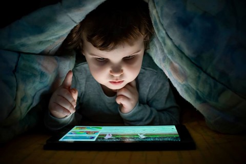Little girl watching her tablet in the bed. Illuminated child face from device screen. Child