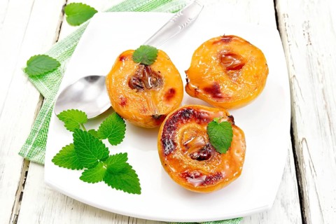 Three halves of quince baked with honey, mint and spoon in a plate on a napkin against a light