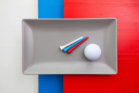Gray ceramic dish with golf equipments on over white, blue and red wooden table, rectangle dish
