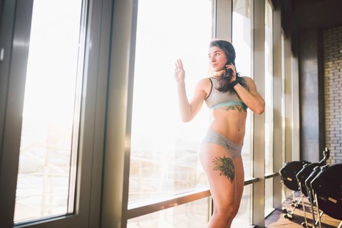Young caucasian sporty woman with curly long hair poses in sportswear near a panorman window in a