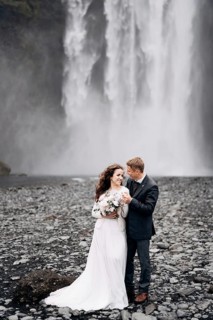 Wedding couple near Skogafoss waterfall. Destination Iceland wedding. The groom hugs the bride by