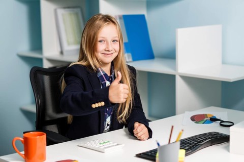 Little girl like business woman sitting at the desk with computer in blue office