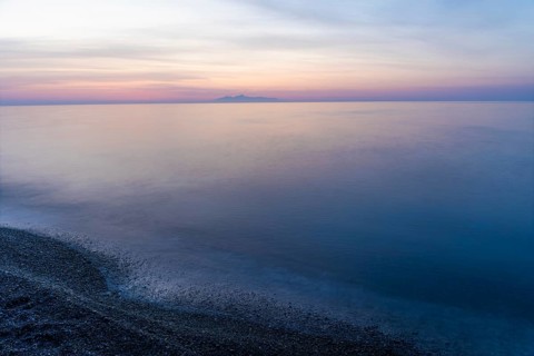 Dawn, cloudy mood in front of sunrise, view from the lava beach to the island of Anafi, long