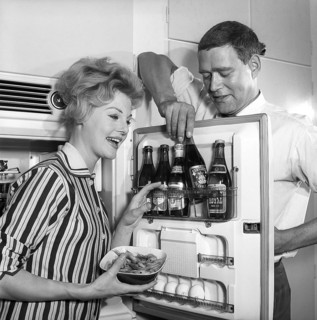 In the kitchen 1950s. A couple in their kitchen and at the refrigerator where the beer is kept in