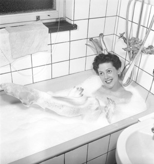 Having a bath 1950. A young smiling woman wearing a princess crown, is having a bath in a bathtub