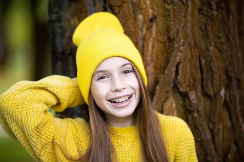 Portrait of modern happy teenage girl with braces dressed in yellow clothes in park. Pretty teenage