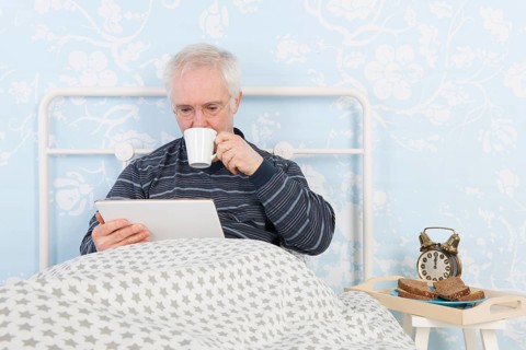 Man reading on digital tablet white having breakfast in bed