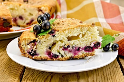 Sweet piece of cake with black currant on a plate, napkin on the background of wooden boards