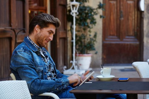 Young man with tablet pc touch in an cafe outdoor having some coffe cup