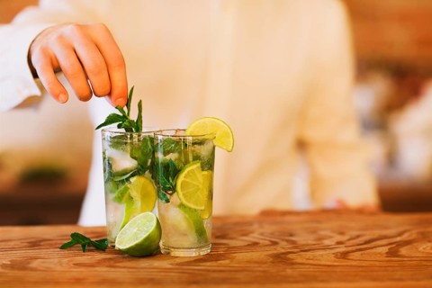 Bartender making two mojito cocktails on wooden bar counter