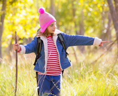 Hiking kid girl with backpack pointing finger in autum poplar trees forest