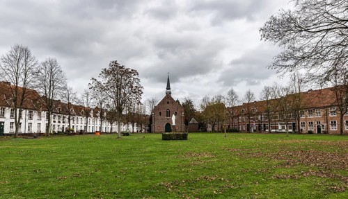 Belgium, 12 08 2018: Old houses and a chapel at the beguinage with bare trees and a meadow during