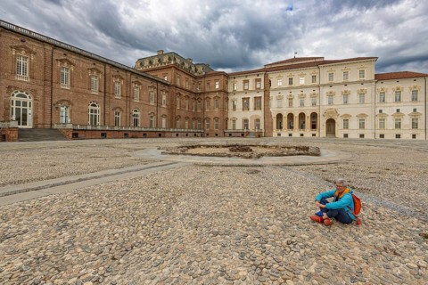 Woman sitting on a pebble square in front of a large building, Palace of Venaria Reale, Residences