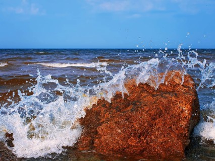 Water splashes over the red rocks against blue sky