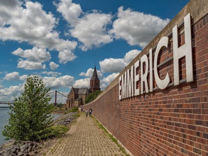 Brick wall and sign of Emmerich, next to it a path along the river on a sunny day, emmerich, lower