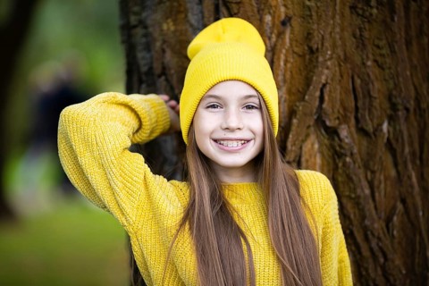 Cute and happy teenage girl with braces smiling at camera in yellow clothes in park. Concept of