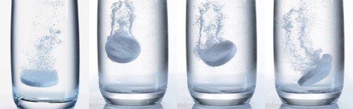 Tablets Falling and Dissolving into a Glass of Water against White Background