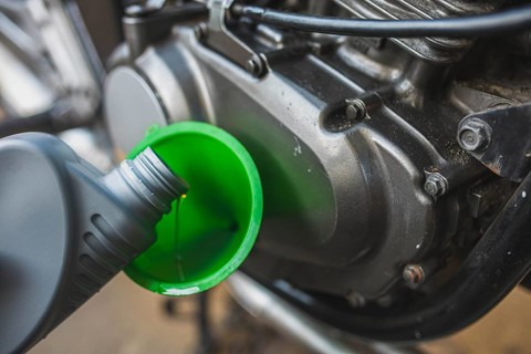 A close-up of a motorcycle engine with oil being poured through a green funnel
