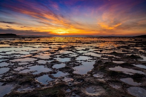 A beautiful sunset over the ocean with rocky beach and tidal pools in the foreground