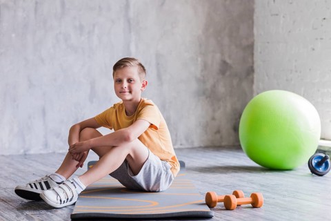 Smiling boy sitting exercise mat with dumbbell pilates ball roller slide