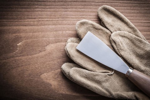 Paint scraper and safety glove on wooden board