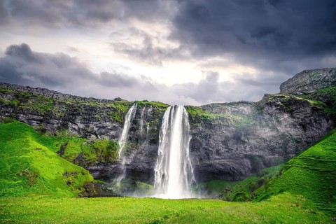 The beautiful Seljalandsfoss waterfall in Iceland surrounded by lava cliffs and green fields in a