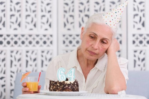 Unhappy elder woman looking her birthday cake holding glass juice hand