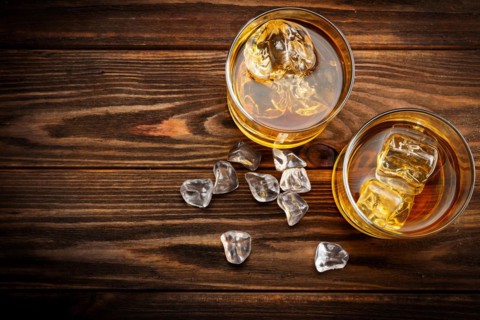Two glasses with ice and whiskey on wooden background (top view)