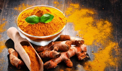 Composition with bowl of turmeric powder on wooden table