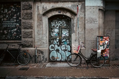 Urban street scene with bicycles and a graffiti-covered door against a weathered brick wall in