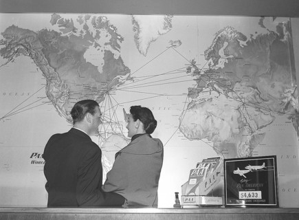 In the 1950s. A young couple at a travel agency stands in front of a world map and looks at all the
