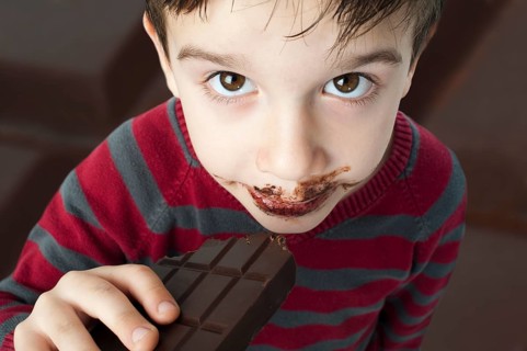 Smiling kid eating chocolate. Smeared stained with chocolate lips