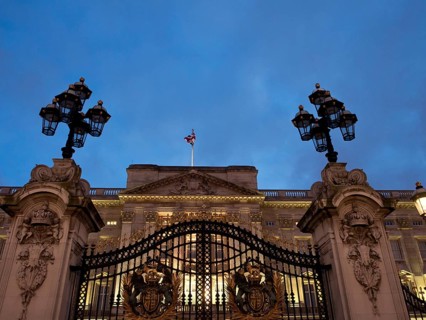 Iron gate with coat of arms and lanterns, illuminated at night in front of a building, London,
