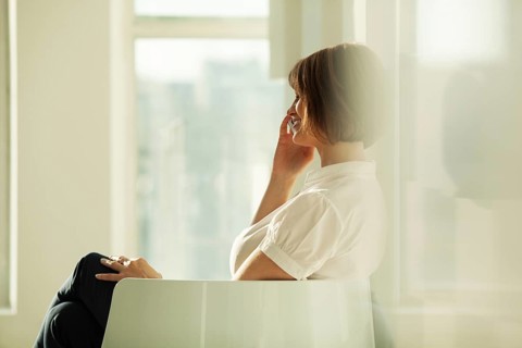 Smiling adult businesswoman talking on smartphone while sitting in chair