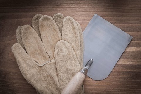 Working safety gloves and bricklaying trowel on vintage wooden background