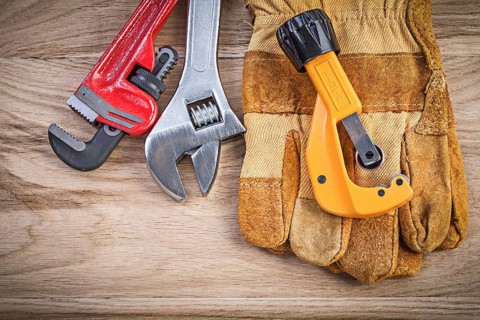 Safety gloves adjustable key monkey wrench pipe cutter on wood board plumbing concept