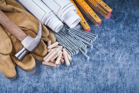 Blueprint rolls claw hammer safety gloves wooden meter metal nails and dowels on scratched metallic