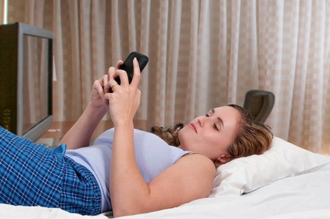 Beautiful young woman texting in bed on her mobile phone