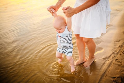 Baby boy walking along beach with mom's support. Mother teaching baby to walk. Outdoor, trust