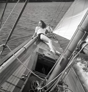 1940s sailing boat. A young woman is aboard a fashionable sailing boat and is lying on deck when it